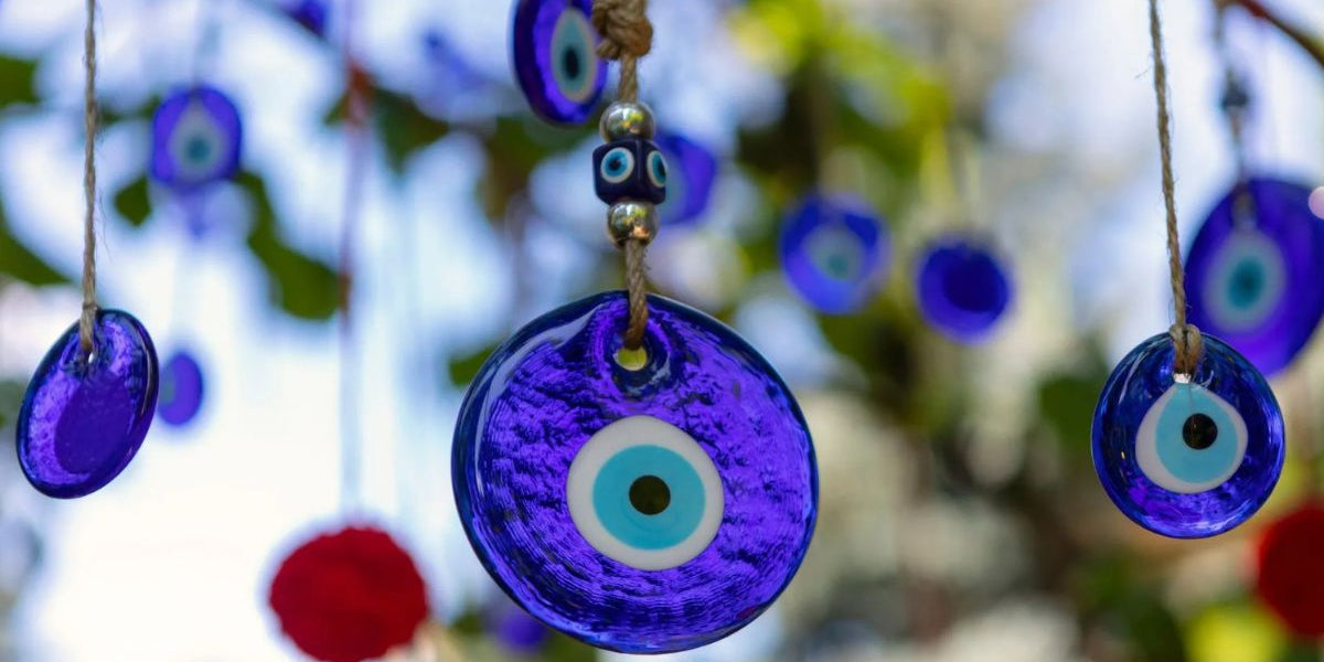 Blue glass evil eye nazar discs hanging on twine among white blossom for buri nazar protection - Divine Sansar UAE