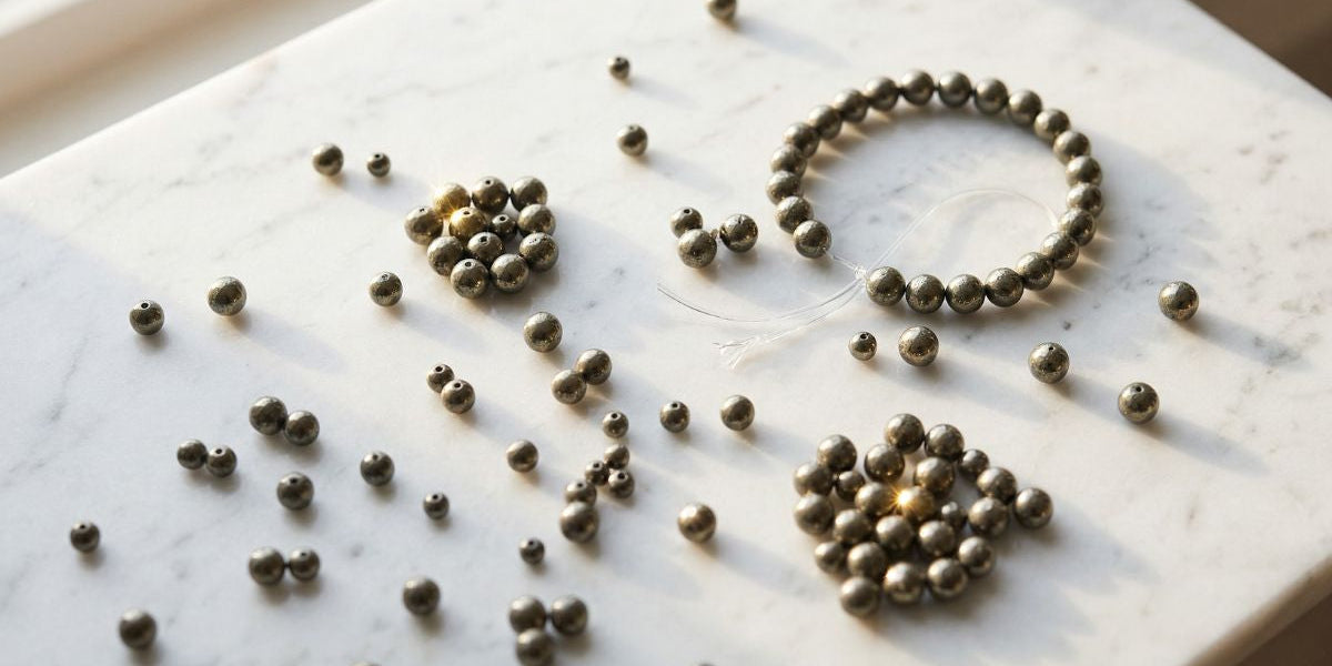 Scattered gunmetal pyrite crystal beads on white marble after bracelet broke - Divine Sansar