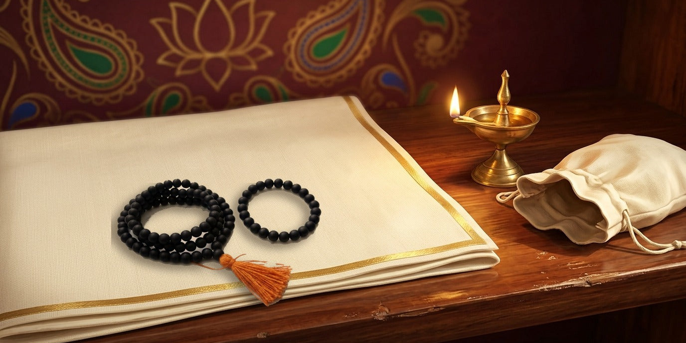 Black Karungali ebony mala coiled with orange tassel beside a matching bead bracelet on a cream altar cloth by a brass lamp - Divine Sansar UAE