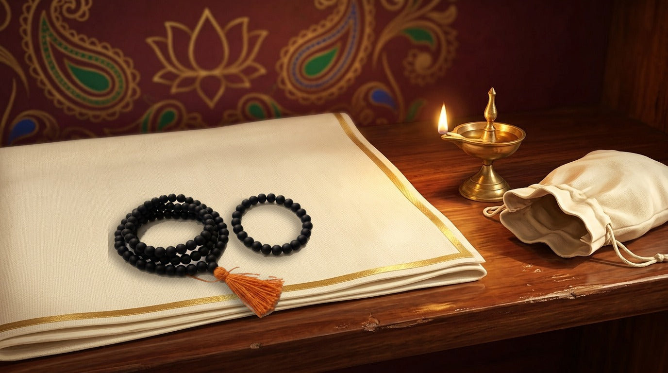Black Karungali ebony mala coiled with orange tassel beside a matching bead bracelet on a cream altar cloth by a brass lamp - Divine Sansar UAE