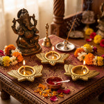 Three lit brass Kamal lotus diyas on a home mandir with Ganesh ji and marigolds - Divine Sansar