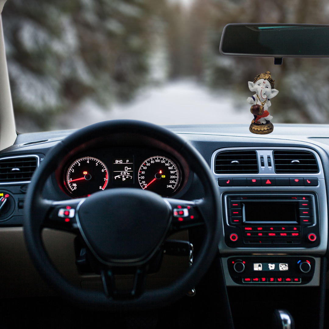 Divine Sansar-Baby Dancing Ganesha-Car interior with dashboard lights on, steering wheel, and Ganesha statue on the dashboard.