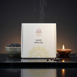 Divine Sansar-Box of Black Urad Dal with a bowl of dal and lit candle on a dark surface