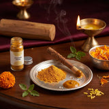 Divine Sansar-Chandan Kesar powder in a bottle and on a plate on a wooden surface with a lit lamp in the background.