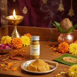 Divine Sansar-Bottle of Chandan Kesar powder on a wooden table with flowers and candles.
