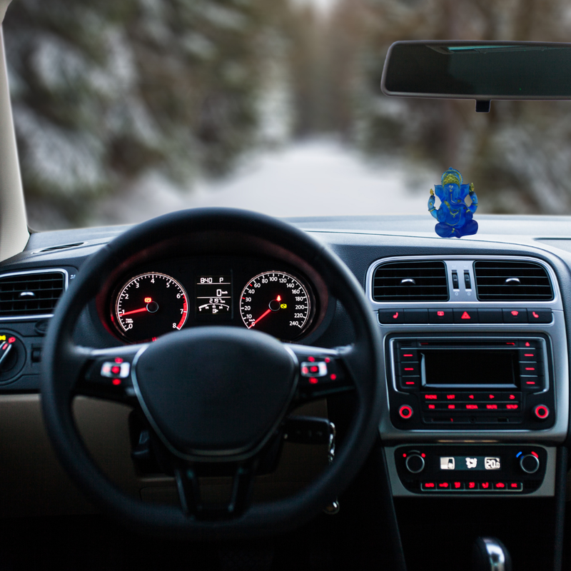 Divine Sansar-Divine Ganesha Statue-Transparent Blue-4 Inches-Car interior with dashboard lights on, steering wheel, and a decorative figure on the dashboard.
