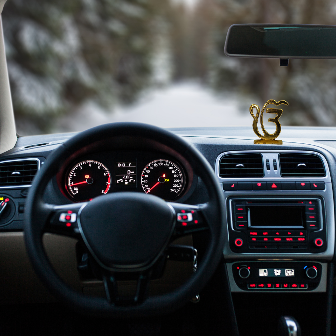 Divine Sansar-Golden Ek Onkar Idol-Car interior with dashboard, steering wheel, and decorative Golden Ek Onkar Idol on a blurred road background