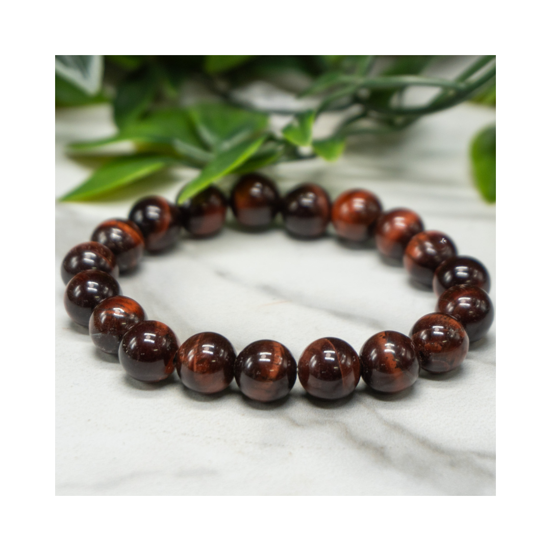 Divine Sansar-Red Tiger Eye Bracelet on a marble surface with green leaves in the background