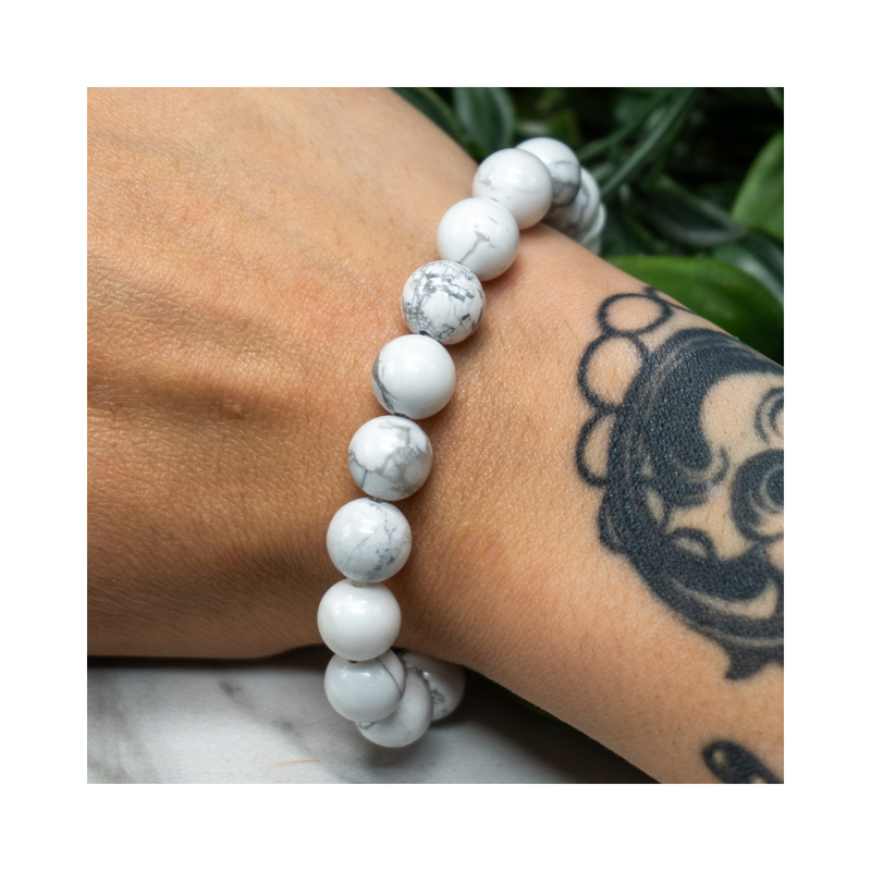 Divine Sansar-Soothing Bracelet: Howlite bracelet on a wrist with a tattoo, against a blurred natural background