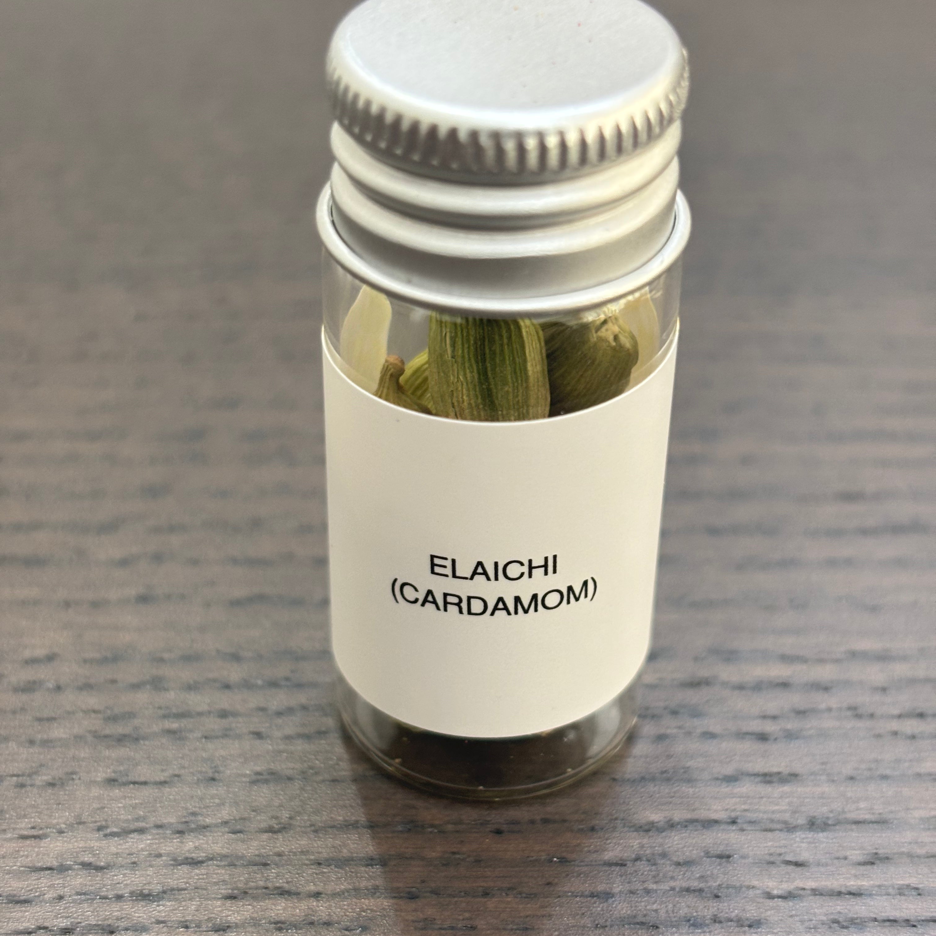 Divine Sansar Elaichi (Cardamom) bottle  with metal lid containing cardamom on a gray surface