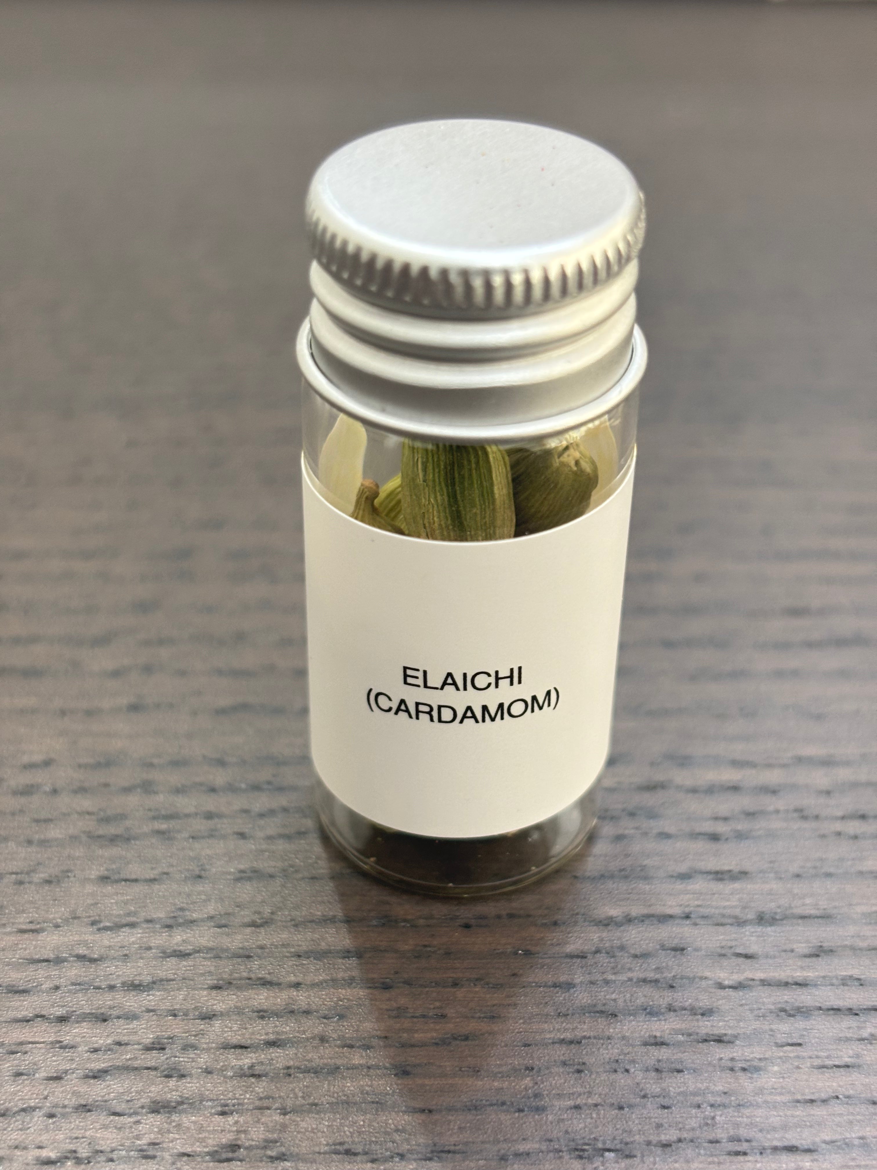 Divine Sansar Elaichi (Cardamom) bottle  with metal lid containing cardamom on a gray surface