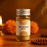 Divine Sansar-Bottle of 'Govardhan Mitti' on a wooden surface with decorative elements and a lit candle in the background.