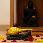 Divine Sansar Hanumanji Gada Golden object on a black rock with flowers and a statue in the background
