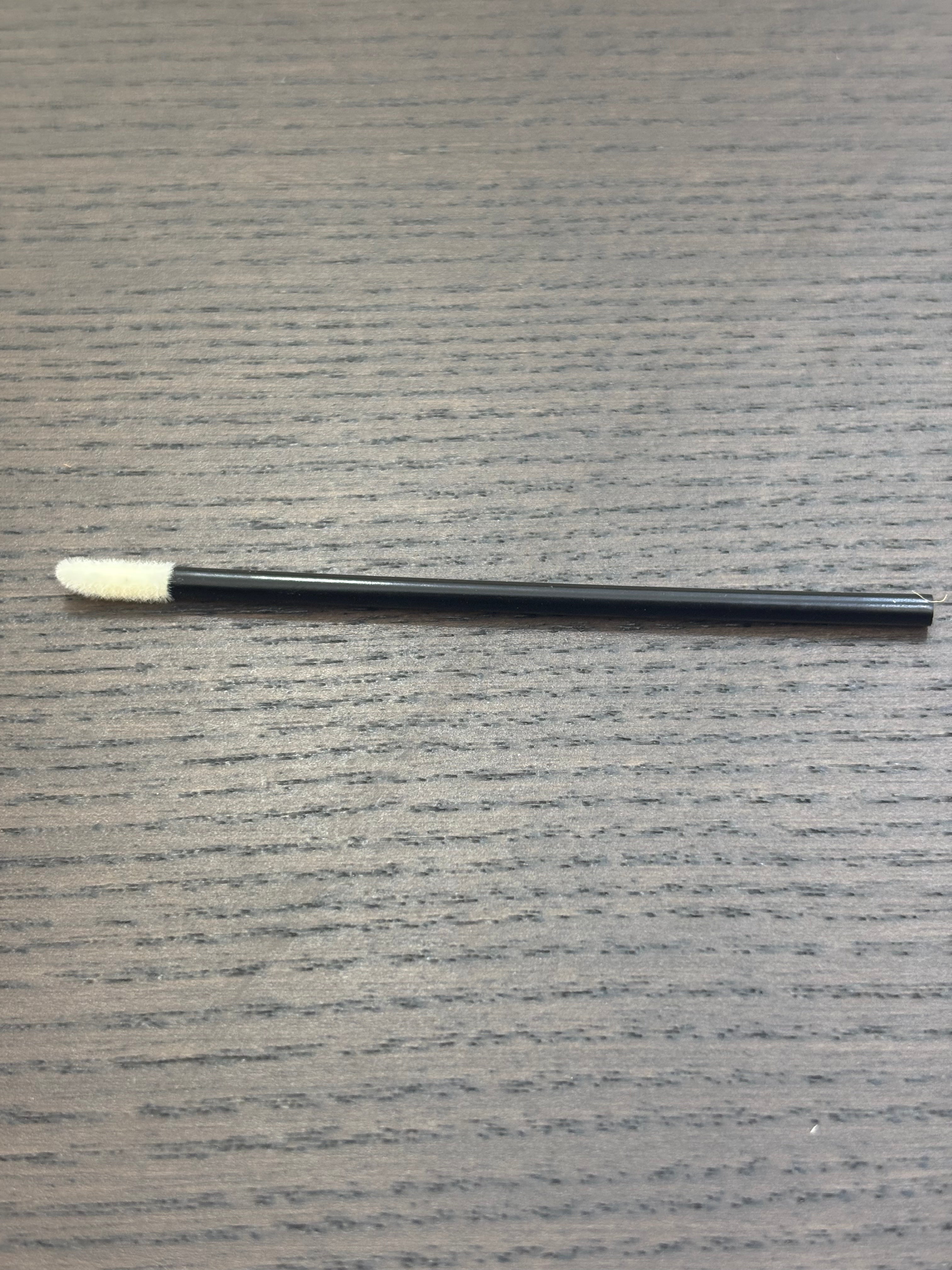 Divine Sansar-Black makeup brush with white bristle tip on a gray textured surface