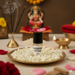 Divine Sansar-Jasmine attar bottle on a decorative plate with incense sticks, flowers, and a statue in the background.