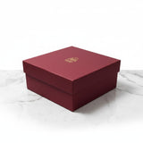 Closed maroon Laxmi Charan gift box with the gold foil lotus logo, Divine Sansar