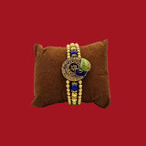 Divine Sansar Meenakari Peacock Rakhi Design 1 brown pillow against a red background