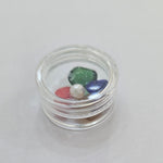 Divine Sansar-Round opaque container with green, red, and clear gemstones on a white background
