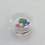 Divine Sansar-Round opaque container with green, red, and clear gemstones on a white background