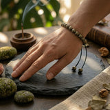 Divine Sansar-Pyrite Braided Money magnet ambiant in a hand-Hand with a Pyrite Braided Money magnet bracelet on a dark surface 