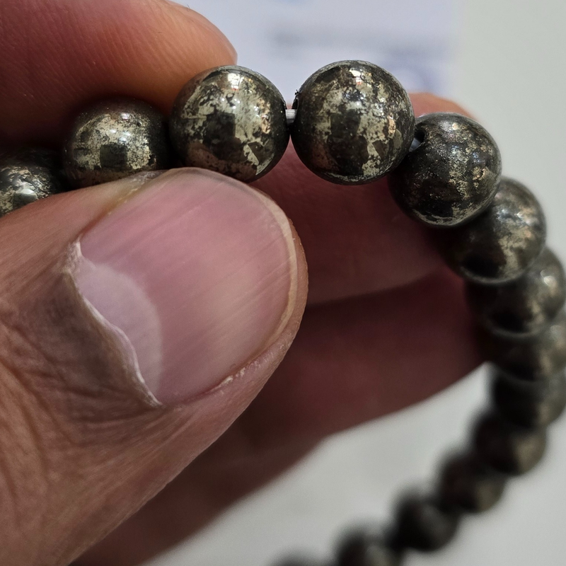 Close-up of natural pyrite beads held between fingers, showing the real mineral texture - Divine Sansar
