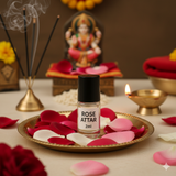Divine Sansar-Rose Attar bottle on a tray with rose petals, incense sticks, and a statue in the background.