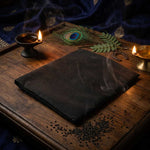 Divine Sansar-Black cloth on a wooden table with candles, peacock feather, and other decorative items.