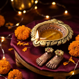 Big clay diya lit with ghee beside a Laxmi Charan pair on a maroon chowki for Diwali Lakshmi Puja - Divine Sansar